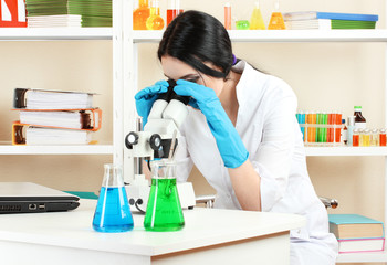 Young female scientist looking at microscope in chemistry