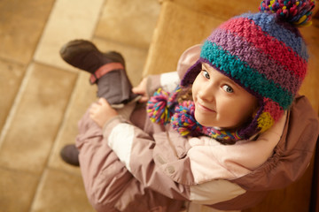 Young Girl Sitting On Wooden Seat Putting On Warm Outdoor Clothe