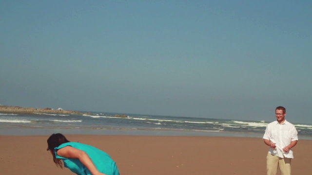 Happy couple having fun with freesby on the beach, slow motion