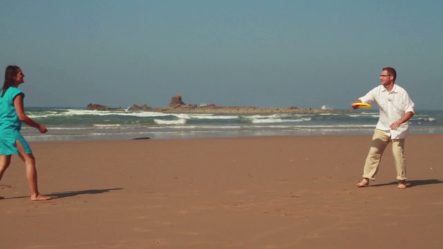 Happy couple having fun with freesby on the beach, slow motion