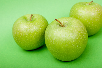 Ripe green apples with water drops on green background