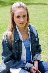 Young serious girl sitting on the grass while looking at the cam