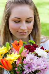 Naklejka premium Young peaceful woman smelling a bunch of flowers while closing h