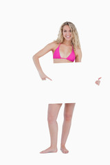 Fototapeta premium Young blonde woman pointing her finger at a blank poster