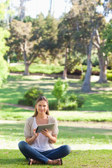 Obraz premium Woman sitting on the lawn while using her tablet