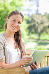 Obraz premium Smiling woman with her tablet on a park bench
