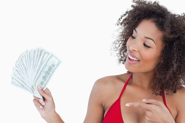 Fototapeta na wymiar Smiling brunette woman pointing a fan of dollar notes