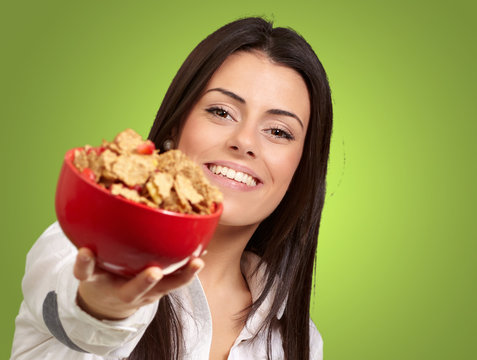 portrait of young woman offering cereals bowl over green backgro