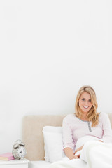 Vertical shot, Woman sitting up against headboard smiling with a