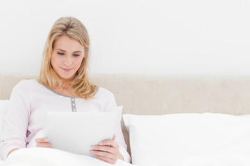 Woman sitting in bed, holding and watching a tablet pc