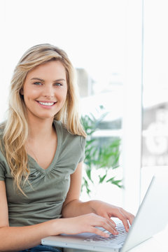 Woman smiling as she uses her laptop on the couch, side view