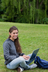 Young woman sitting cross-legged on the grass while using her la