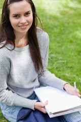 Obraz premium Smiling young girl sitting in a park while looking at the camera