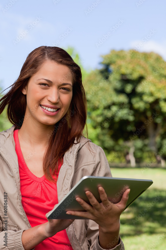 Poster woman smiling and looking ahead while she uses a tablet in a par