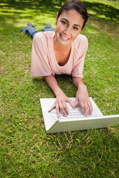 Woman looking ahead while using a laptop as she lies down in gra