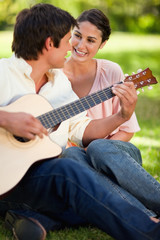 Woman smiling while her friend plays the guitar