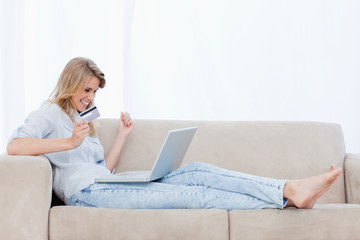 An excited woman holding a bank card has a laptop on her legs