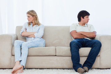 A couple sit at the two ends of the couch with their arms folded