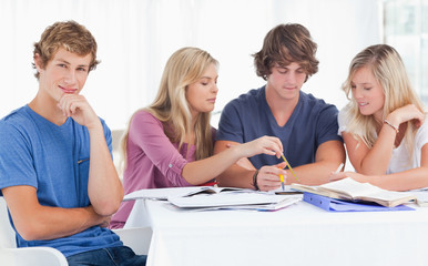 Four friends studying as one guy looks at the camera and smiles