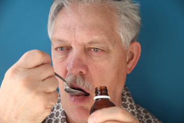 sick older man takes liquid medicine