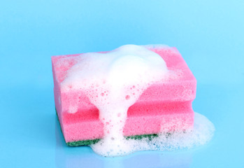 Sponge with foam of dishwashing liquid on blue background