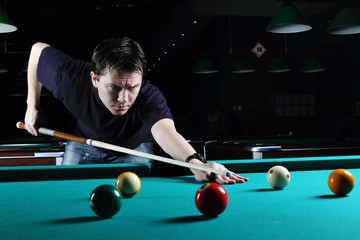 Man learning to play snooker in the dark club.