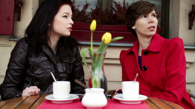 Two female friends chatting in outdoor cafe, steadicam shot