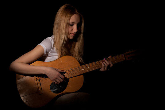The girl plays the guitar on a black background.
