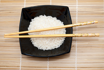 Black bowl with rice and chopsticks on an asian bamboo mat