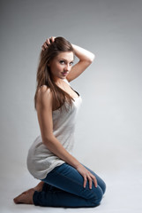 Beautiful young woman sitting in jeans on gray background