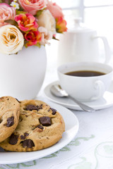 Chocolate chip cookie  on white plate with black coffee and flow