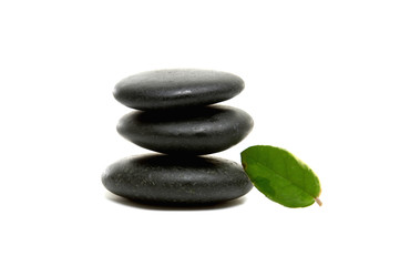 Balanced black zen pebbles and a young green leaf