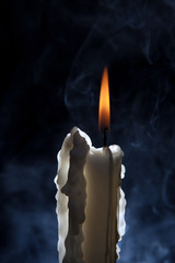 White candle burning with smoke in background