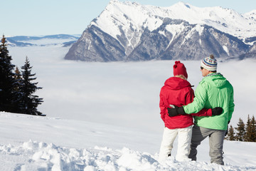 Fototapeta na wymiar Couple Admiring Mountain View Whilst On Ski Holiday In Mountains