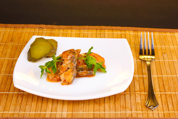Tasty sardines on plate on wooden mat on brown background