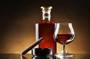 bottle and glass of brandy and cigar on brown background