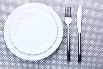 White empty plates with fork and knife on a grey tablecloth