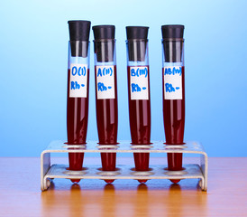 Test-tubes with blood on wooden table on blue background