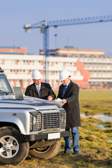 Two architects at  construction site review plans