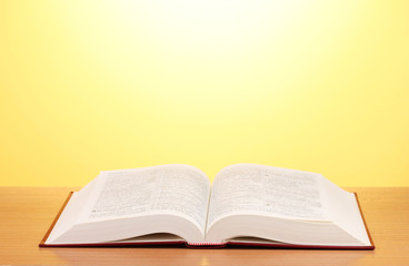 Open book on wooden table on yellow background