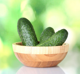 Cucumbers in a wooden bowl on green background