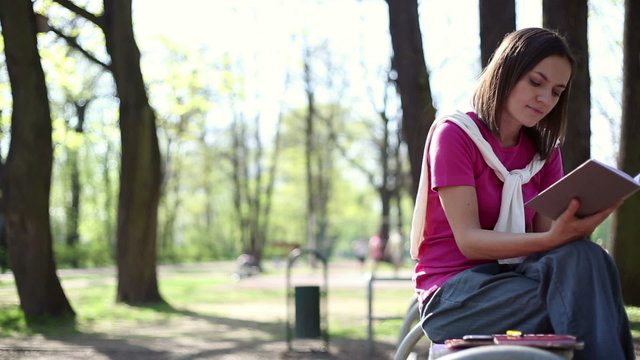 Young attractive girl reading book on park bench, dolly shot
