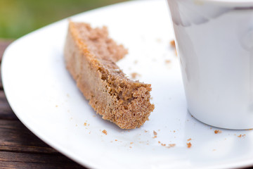 A piece of bread on the plate next cup of coffee