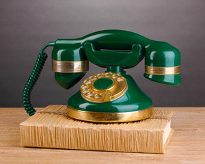 Retro phone standing on book on wooden table on grey background
