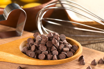 Chocolate chips on wooden spoon with baking utensils