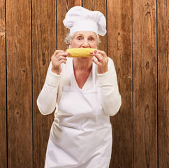 portrait of senior cook woman eating corn cob over wooden wall
