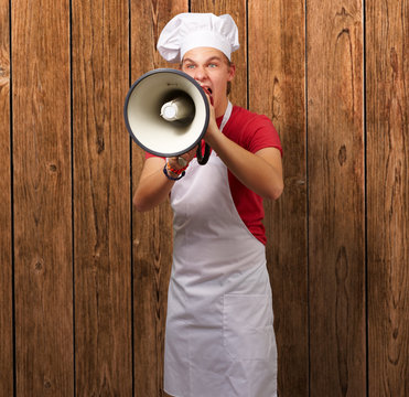 portrait of young cook man screaming with megaphone against a wo