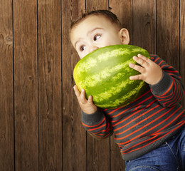 Fototapeta premium portrait of a handsome kid holding watermelon and sucking agains