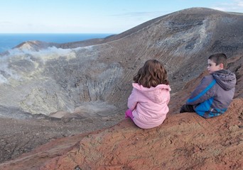 Girl and boy sitting on rim of volcano crater near Sicily