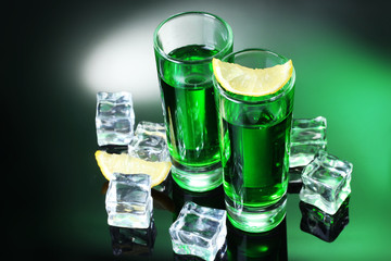 Two glasses of absinthe, lemon and ice on green background